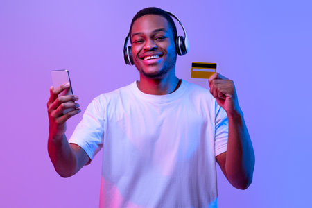 Streaming Music Subscription. Happy black guy in headphones holding smartphone and cardの写真素材