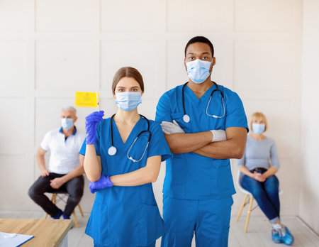 Male and female doctors wearing uniforms and face masks, holding syringe with coronavirus vaccine at clinicの写真素材