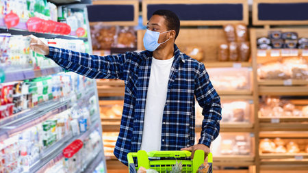 Young black man in protective mask buying dairy products at supermarket during coronavirus...