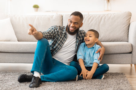 African Father And Son Hugging Sitting On Floor At Homeの写真素材