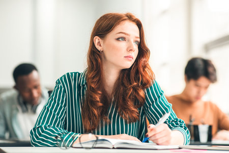 Focused female student sitting at desk in classroom thinkingの写真素材
