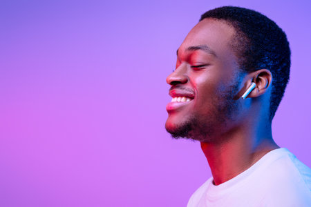 Relaxed African Man Listening Music In Wireless Airpods Earphones In Neon Lightの写真素材