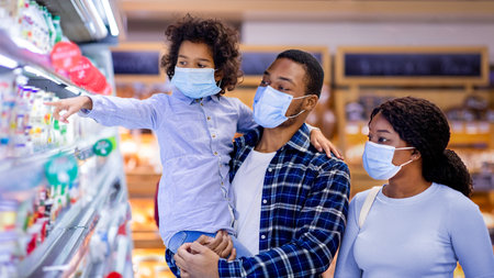 Millennial black family wearing protective masks while shopping for milk products at dairy section of modern supermarketの写真素材