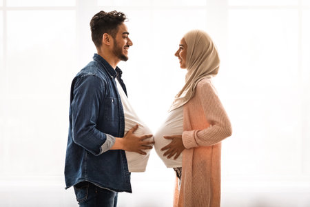 Pregnant islamic lady in hijab comparing belly sizes with her husbandの写真素材