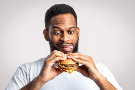 Hungry Black Man Holding Tasty Burger Standing On White Backgroundの写真素材