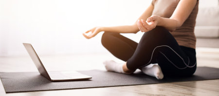 Balanced mature woman meditating with closed eyes in front of laptop at home, selective focusの写真素材