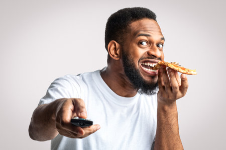 African Guy Eating Pizza And Watching Television On White Backgroundの写真素材