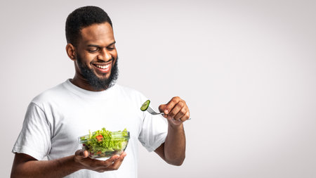 Happy African American Man Eating Salad Standing Over White Backgroundの写真素材