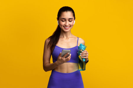 Sporty woman holding bottle with water using smartphoneの写真素材