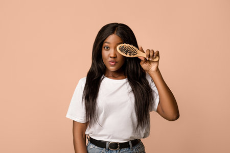 Attractive black woman holding wooden hair brush, covering eyeの写真素材
