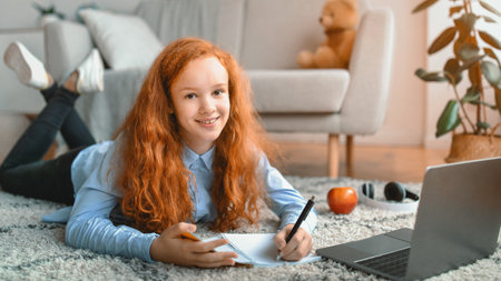Girl lying on floor carpet, using laptop, writing in notebook