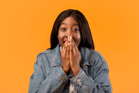Amazed black lady in jeans jacket covering her mouth