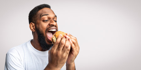 African Man Eating Burger Greedily Enjoying Fastfood Over White Background