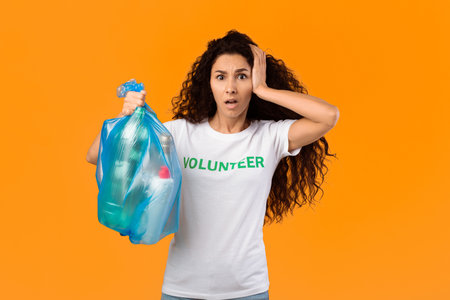 Shocked Volunteer Woman Holding Plastic Bag With Litter, Yellow Backgroundの写真素材