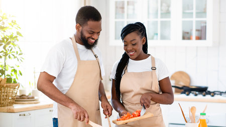 Vegan Diet. Happy young black couple cooking vegetable salad together in kitchen