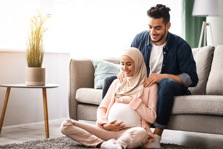 Caring arab husband making shoulder massage for pregnant muslim wife at homeの写真素材