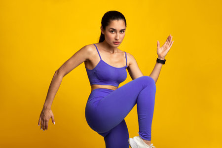 Young Woman Doing High Knees Exercise Isolated On Orange Background