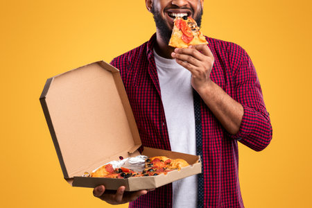 African Man Eating Pizza Smiling To Camera Over Yellow Backgroundの写真素材