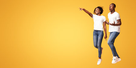 Excited black man and woman jumping, pointing at empty space