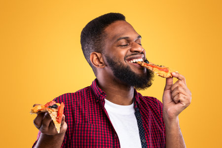 Black Guy Eating Pizza Slice With Eyes Closed, Yellow Backgroundの写真素材