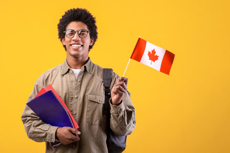 Happy young african american guy in glasses holding notepads and small Canada flag and ready to studyの写真素材