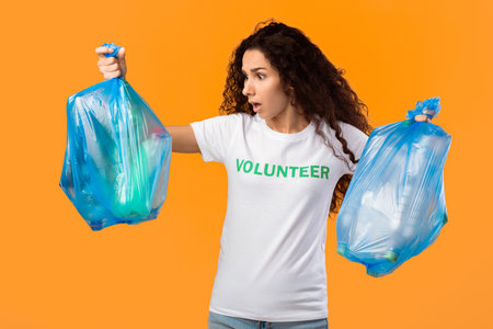 Shocked Female Volunteer Holding Unsorted Plastic Garbage, Over Yellow Background