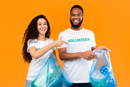 Multicultural Volunteers Picking Plastic In Garbage Bags Over Yellow Backgroundの写真素材