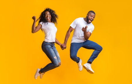 Joyful african couple having fun over yellow background
