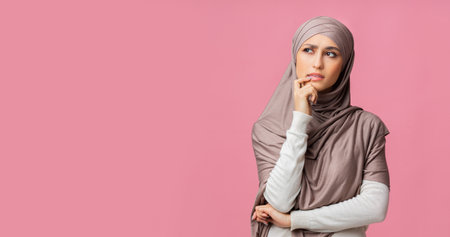Pensive muslim girl thinking and looking away on pink studio backgroundの写真素材