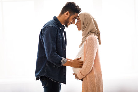 Loving pregnant muslim couple bonding together at home, standing near windowの写真素材
