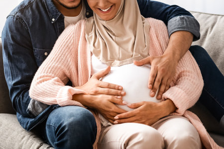 Happy Pregnant Muslim Couple Relaxing On Couch At Homeの写真素材