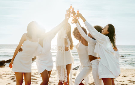 Group of ladies drinking champagne while having a hen party on the beach, women hanging out on coastlineの写真素材