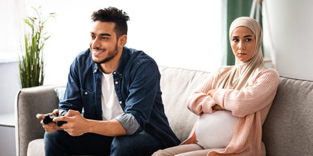Upset Expectant Muslim Woman Sitting Offended To Husband That Playing Video Gamesの写真素材