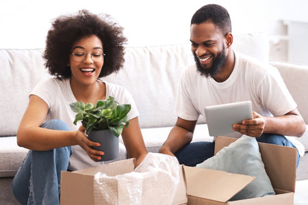 Cheerful Black Spouses Packing Moving Boxes Together Sitting Indoorsの写真素材