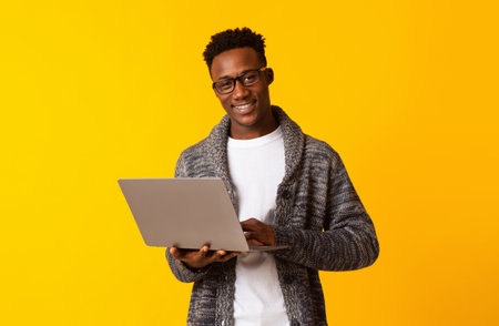 Handsome young african man using laptop on yellow
