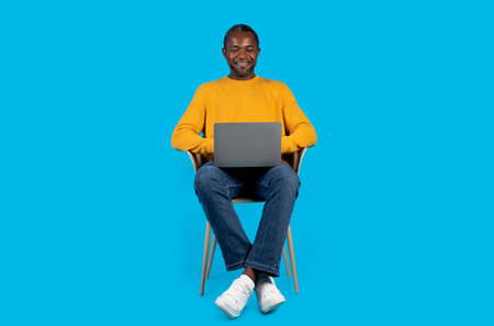Happy african american adult man using laptop on blue