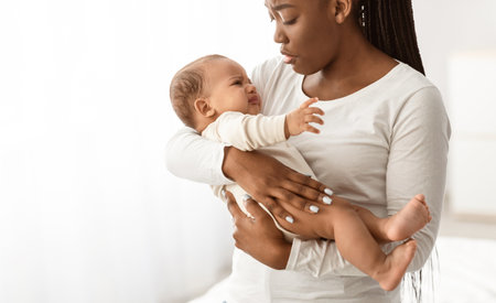 Black mother holding crying baby with colic on hands