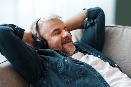 Happy mature man laying on couch, listening to music