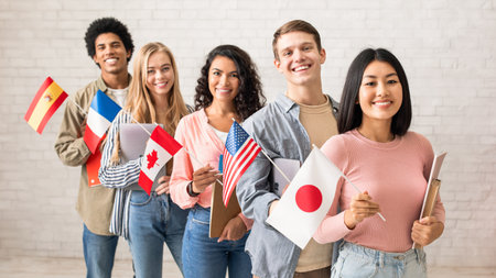 International multi-ethnic student exchange. Cheerful young people with devices and books look at cameraの写真素材