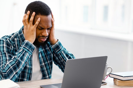 Stressed Black Businessman Having Headache Sitting At Workplace In Office