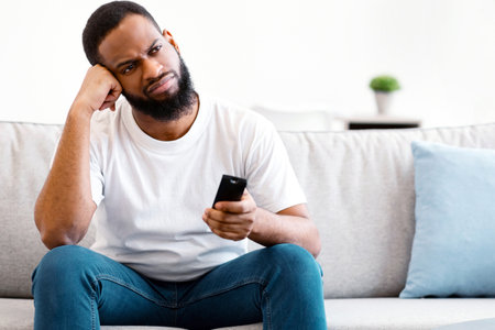 Bored African American Guy Watching Boring Television Program At Homeの写真素材