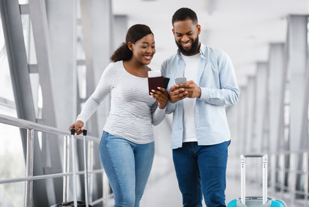 Happy black couple using phone at airport