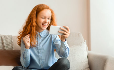 Cheerful excited girl using her cell phone sitting on couchの写真素材