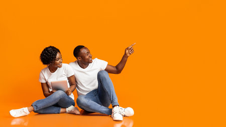 Excited black couple with digital tablet pointing at copy spaceの写真素材