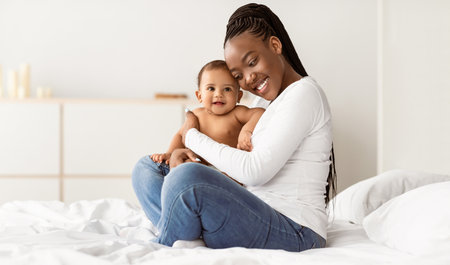 Black mom sitting on bed with her cute babyの写真素材