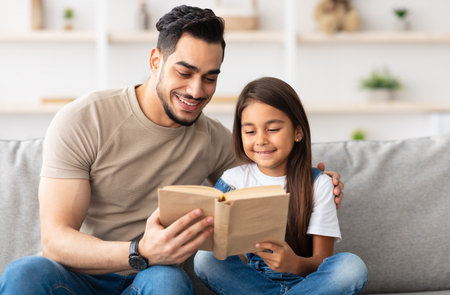 Dad and daughter reading book spending time together at homeの写真素材