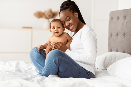 African American mom sitting on bed with her cute baby