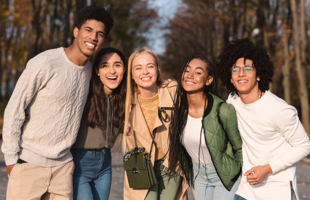 Cheerful multiethnic teenagers embracing and smiling at camera outdoorsの写真素材