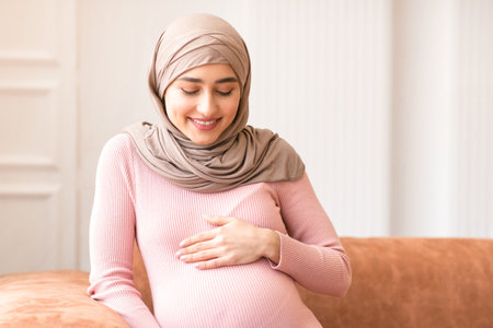 Pregnant Muslim Lady In Hijab Posing Sitting On Couch Indoorの写真素材