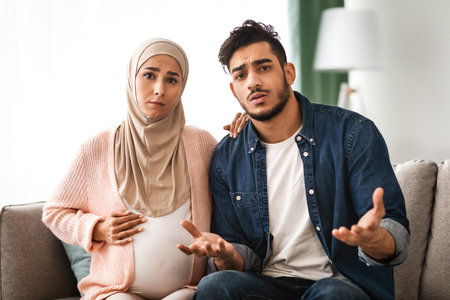 Portrait Of Worry Arab Man And Pregnant Muslim Wife Talking At Cameraの写真素材